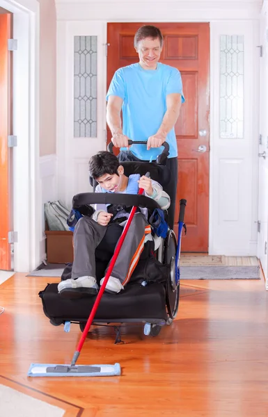 Père aidant fils handicapé en fauteuil roulant balayez le sol — Photo