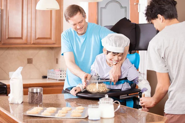 Chico discapacitado en stander horneando galletas con padre y hermano — Foto de Stock