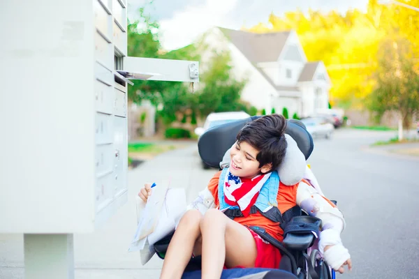 Bambino disabile in sedia a rotelle che riceve posta dalla casella di posta — Foto Stock