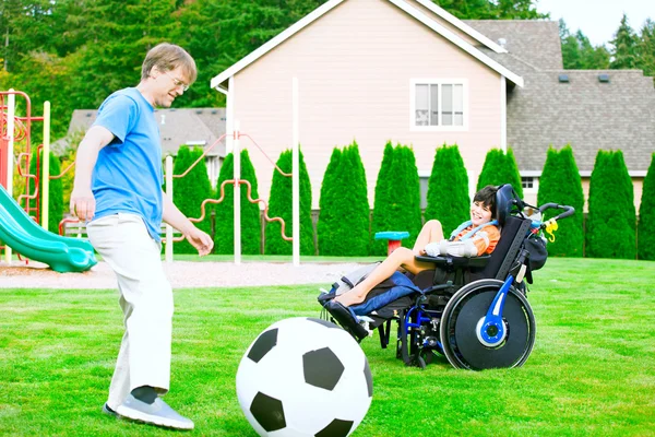 Отец играет в футбол с сыном-инвалидом в инвалидном кресле в парке — стоковое фото