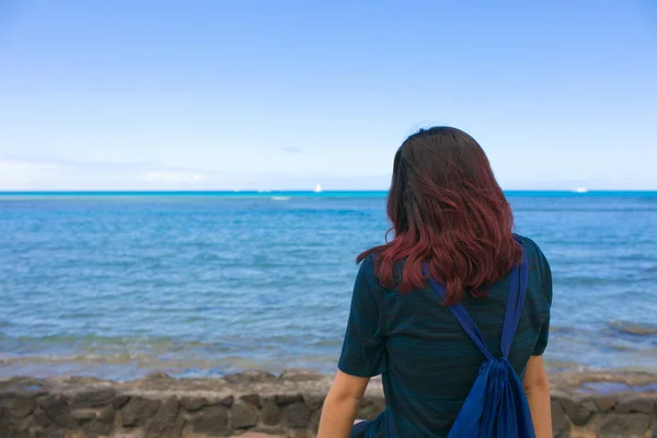 夏威夷热带蓝海旁边的水泥人行道上坐着一个年轻的女孩 她的背景是蓝天蓝天蓝天蓝天 — 图库照片