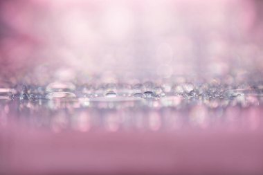 Su damlaları pembe yüzeyde ışıldıyor ve parlıyor, soyut bir arka plan.