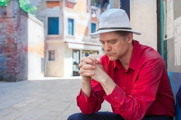 在意大利 身穿红衫 头戴白帽的白人男子坐在室外祈祷 闭上眼睛 — 图库照片