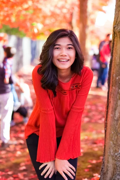 在公园红枫树下 身穿红衫的少女微笑着 — 图库照片