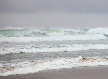 Pasifik okyanusunun güzel zümrüt yeşili dalgaları sisli bir günde alacakaranlıkta kıyıya vuruyor.