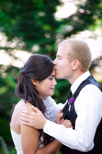 Kaukasiska brudgummen omsorgsfullt kysser sin biracial brud på kinden. Di — Stockfoto