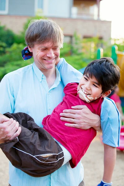 Caucasiano pai carregando biracial filho deficiente no parque infantil — Fotografia de Stock