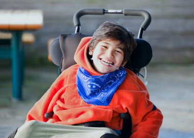 Wheelchai içinde gülümseyen yakışıklı, mutlu biracial sekiz yaşında bir çocuk
