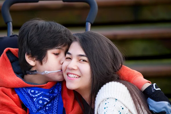 Маленький мальчик-инвалид целует свою старшую сестру в щеку, сидя — стоковое фото