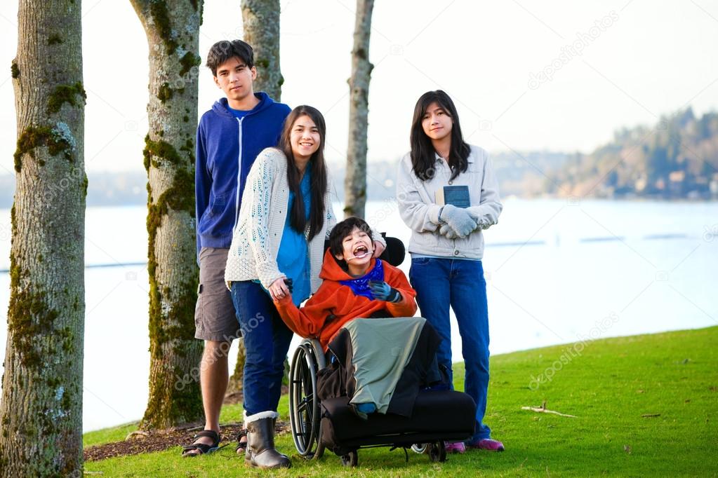 Disabled little boy in wheelchair surrounded by brother and sist