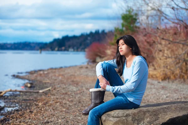 Jeune adolescente en chemise bleue et jeans assis le long du lac rocheux — Photo