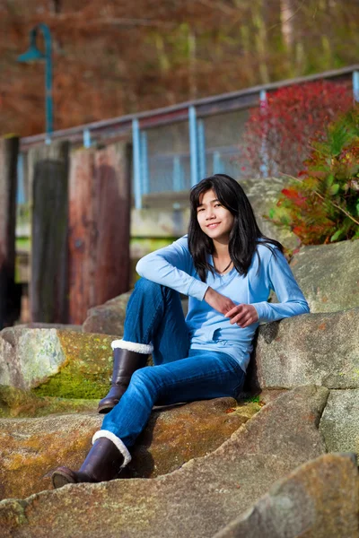 Young teen girl relaxing on large boulder along lake shore, smil — Stock Photo, Image