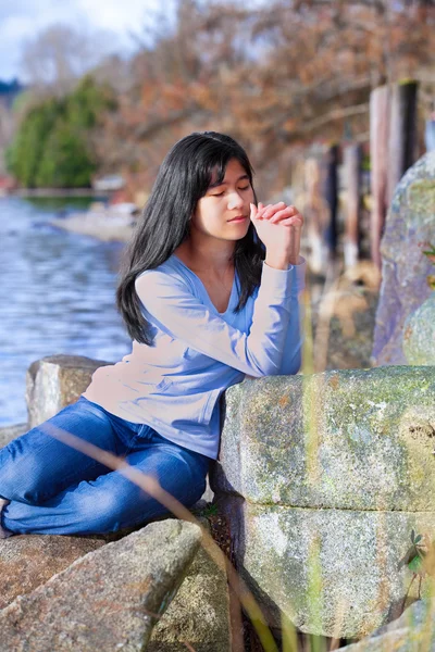 Giovane ragazza adolescente seduta all'aperto su rocce pregando — Foto Stock