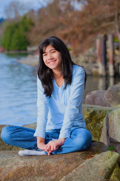 Genç genç kız Gölü kıyısında, SMIL büyük kayanın üzerinde rahatlatıcı — Stok fotoğraf