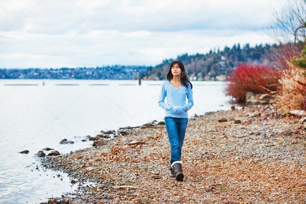 Young teen girl walking along rocky shoreline of lake in early s