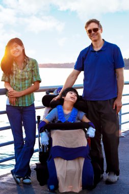 Disabled child in wheelchair outdoors by lake with family