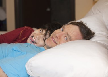Father sleeping in bed with disabled young son, laughing and smi clipart