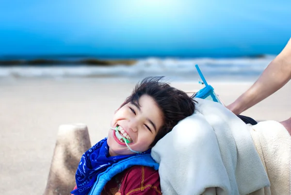 Happy disabled boy being pushed in wheelchair with ocean beach i — Stock Photo, Image