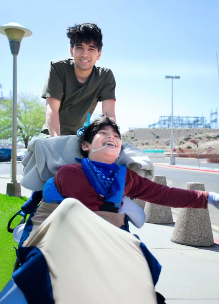 Big brother pushing happy disabled boy in wheelchair — Stock Photo, Image