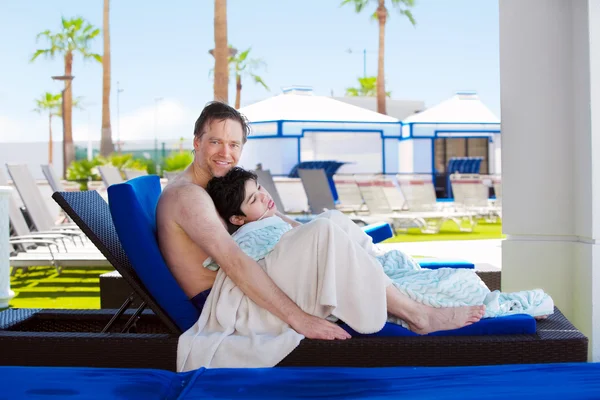 Father drying off on blue lounger with disabled son off side of — ストック写真