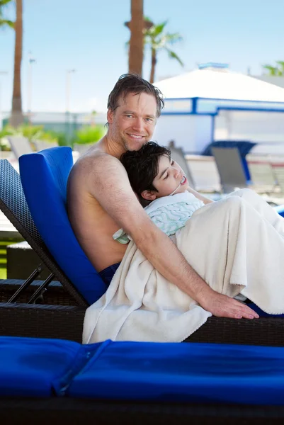 Father drying off on blue lounger with disabled son off side of — Zdjęcie stockowe