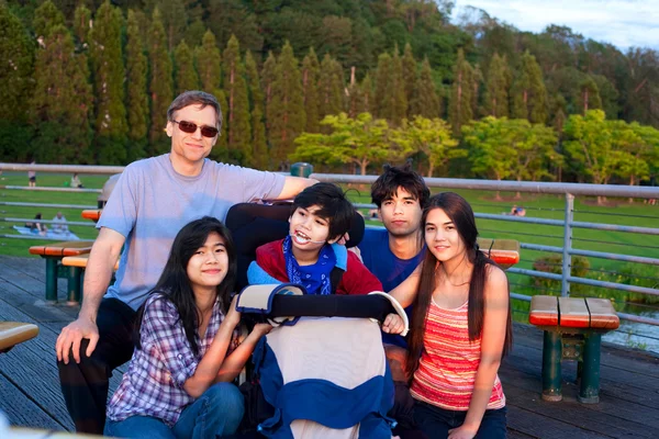 Father with children at park, surrounding disabled son in wheelc — Stock fotografie