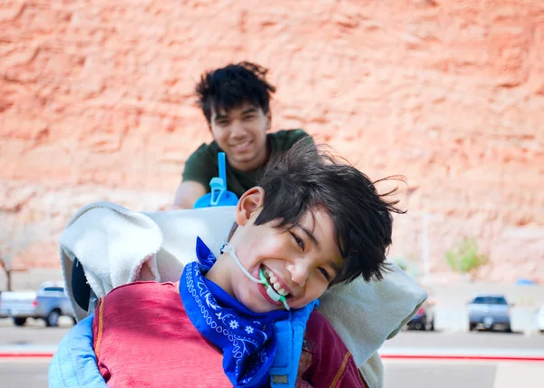 Big brother pushing happy disabled boy in wheelchair Stockfoto