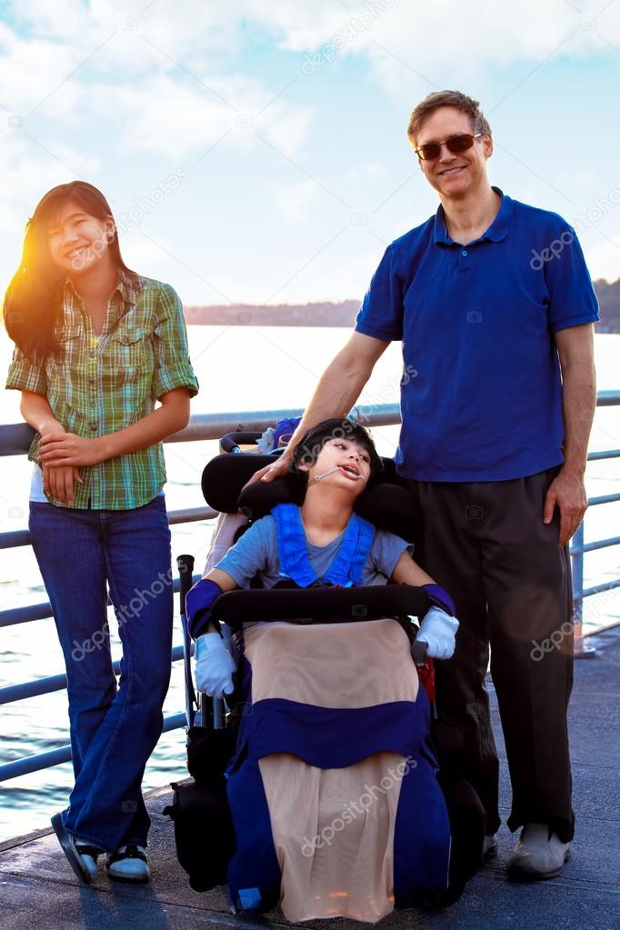 Disabled child in wheelchair outdoors by lake with family