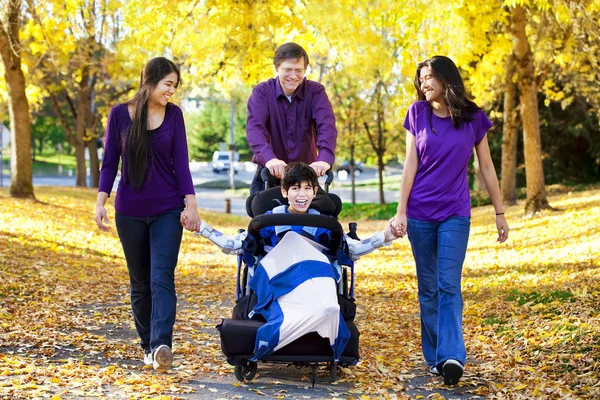 Familia con niño discapacitado en silla de ruedas caminando entre otoño le —  Fotos de Stock