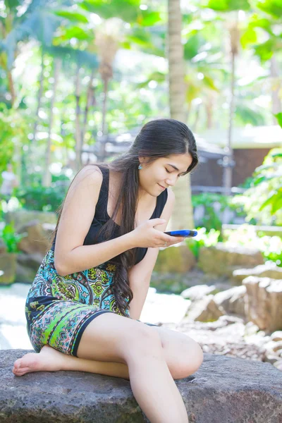 Biracial teen ragazza seduta sulla roccia guardando il cellulare — Foto Stock