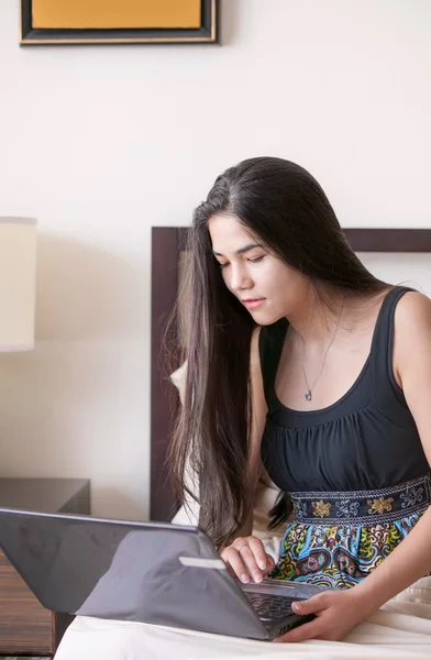 Birassisch teen girl sitting im bett studying on laptop computer — Stockfoto