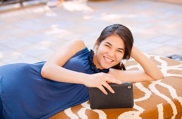 Biracial adolescente chica acostada en el banco al aire libre utilizando tableta ordenador — Foto de Stock