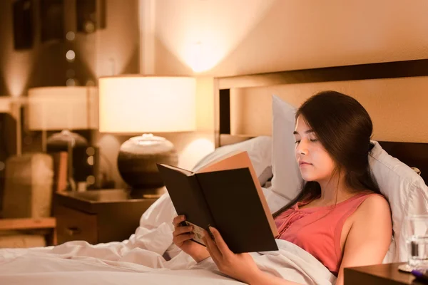 Biracial adolescente chica leyendo libro en la cama por la noche — Foto de Stock