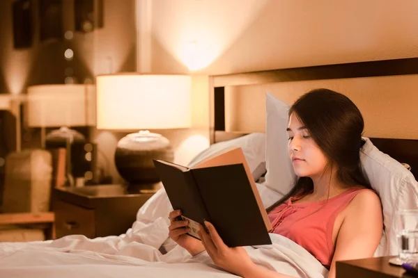 Biracial teen mädchen reading buch im bett bei nacht — Stockfoto