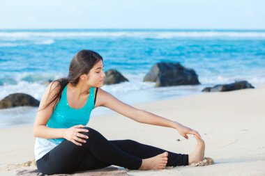 Teen girl exercising on sandy beach of Hawaii near ocean