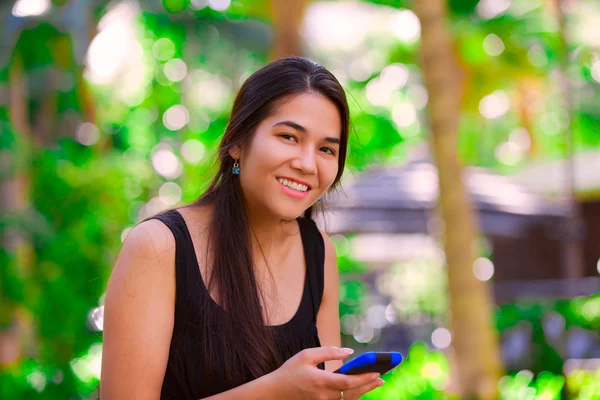 Biracial adolescent fille à l'aide de téléphone portable dans un cadre tropical — Photo