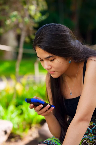 Biracial teen girl looking at cellphone in tropical setting — Stockfoto