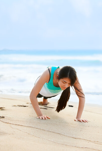 Teen girl exercising on beach near blue ocean waters
