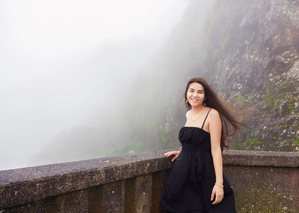 Teen girl standing on foggy hillside in black dress,  smiling — Stockfoto