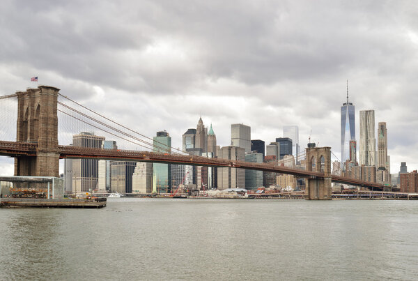 Manhattan skyline with Brooklyn Bridge at cloudy day.