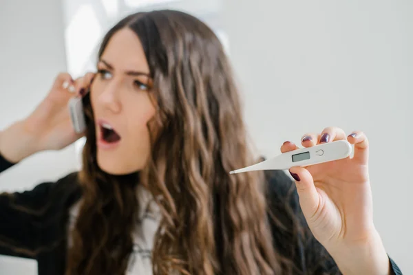 Kvinna med termometer och telefon — Stockfoto