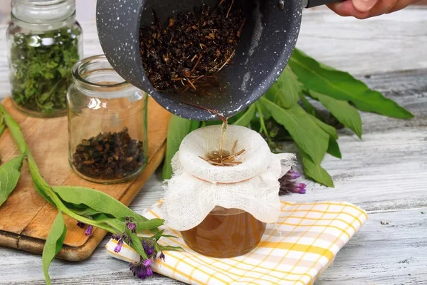 Alternative medicine, filtering comfrey ointment good for bones, decorated with fresh comfrey and dried comfrey roots — Stock Photo, Image