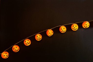 Cadılar Bayramı geçmişi. Siyah kağıtta balkabağı olan turuncu ışıklı çelenk. Mutlu Cadılar Bayramı konsepti. Kutlama kartı, Cadılar Bayramı için festival arkaplanı. Düz yatış, üst görünüm.