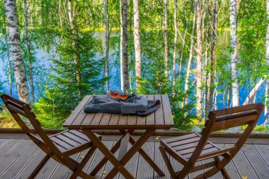 Panoramik kulübeden dışarıdaki terasa masa ve sandalyelerle kuzey ormanlarındaki güzel göl manzarasına bakın. Masadaki kazağa sarılı alkollü bardaklar. Kalma.