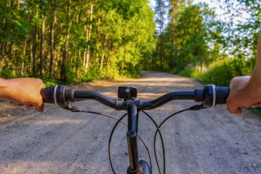 İnsan eli bisiklet gidonunu kır yolu manzarasına karşı tutuyor. Yaz akşamı kuzey ormanında bisikletle seyahat eden bir adam. Hafta sonu aktiviteleri, sağlıklı yaşam tarzı, macera konsepti. POV