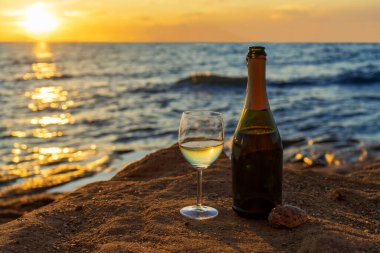 Gün batımında muhteşem deniz manzarasına karşı şampanya şişesi ve köpüklü şarap kadehi. Deniz manzarasında alkollü güzel bir hayat. Yaz tatili, deniz konseptinde hafta sonu.