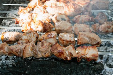 Kömürün üzerine yerleştirilmiş metal şişler üzerinde ızgara et parçaları.