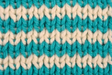 A macro close-up captures a chunky knitted textile pattern featuring horizontal teal and off-white chevron stripes