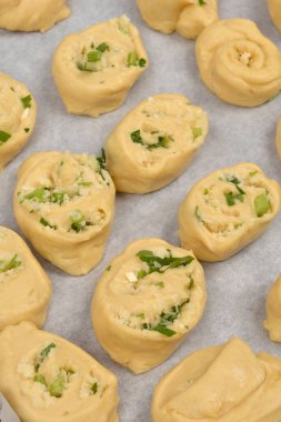A close-up shows several unbaked dough rolls filled with Parmesan cheese, garlic, and green herbs, resting on parchment paper