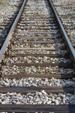 A straight section of railroad tracks extends into the distance, featuring metal rails, wooden sleepers, and bright gravel ballast in a close-up perspective